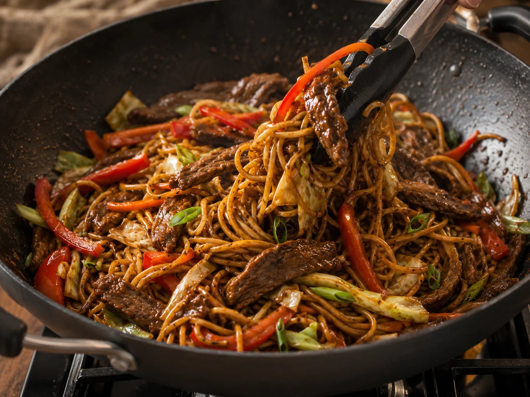 Beef chow mein noodles being tossed in a wok with vegetables